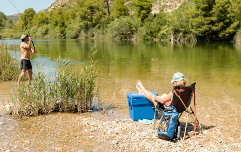 Eine Frau mit einem Mann am See beim Angeln, die Füße auf der Qool Kühlbox