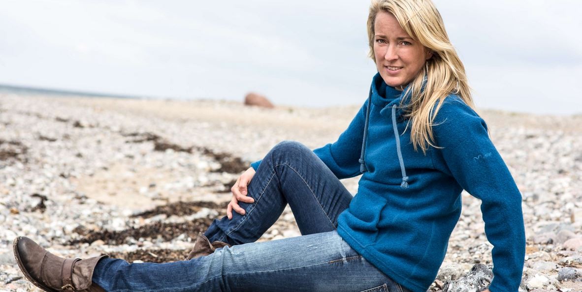 Frau mit Mufflon Jacke sitzt an einem Strand