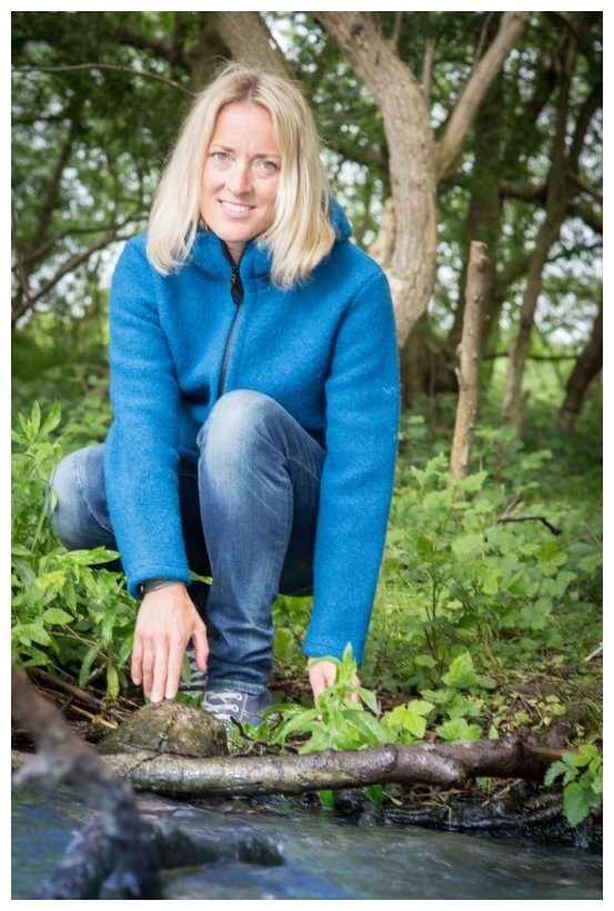 Eine blonde Frau kniet vor einem Fluss