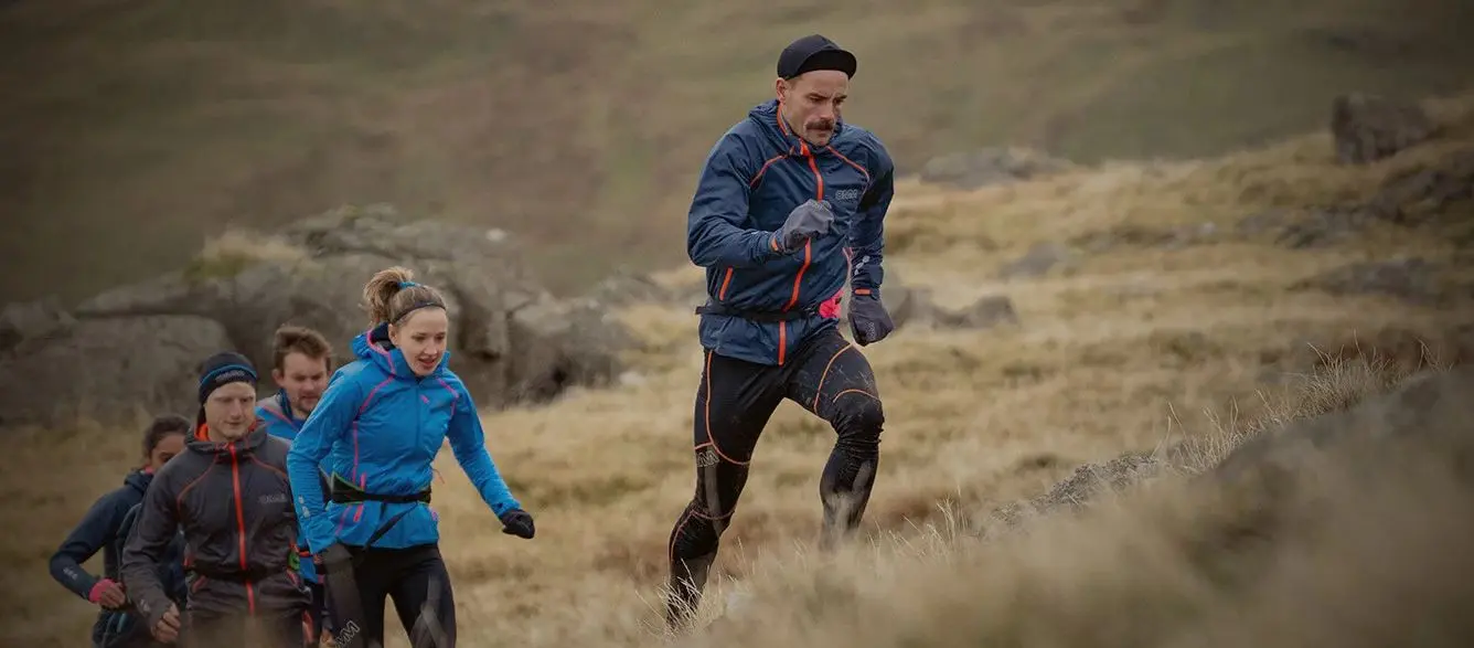 Eine große Gruppe von Joggern in OMM Kamleika Bekleidung läuft einen Berg hinauf